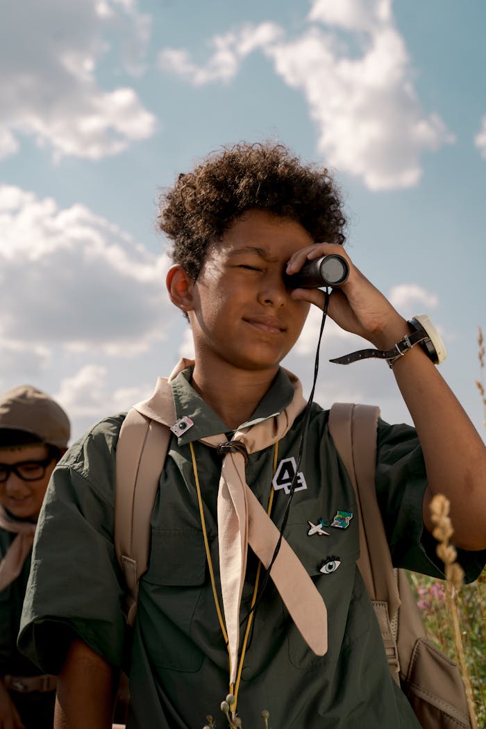 A young scout looks through binoculars during a sunny day at summer camp.