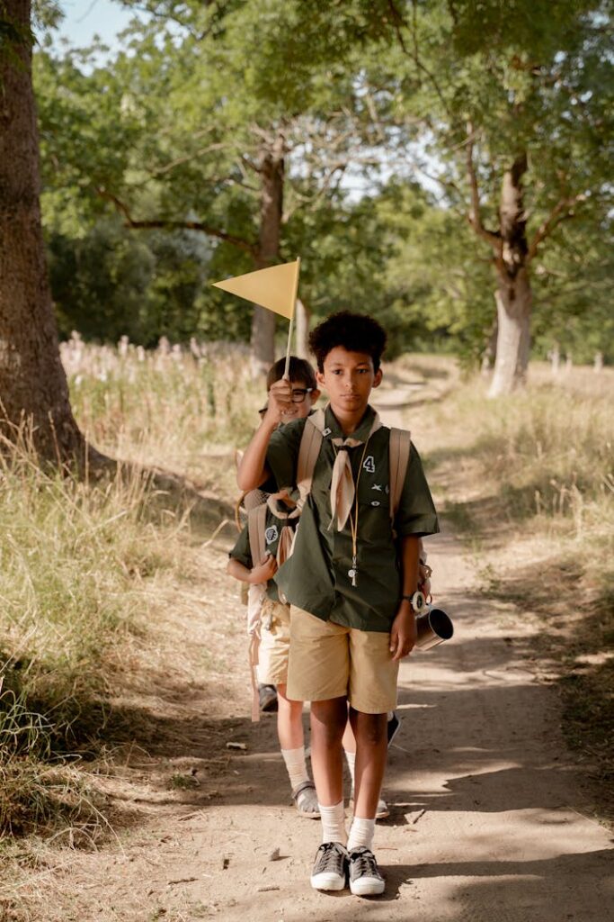 Three young scouts in uniform hiking along a forest trail holding a flag on a sunny day.