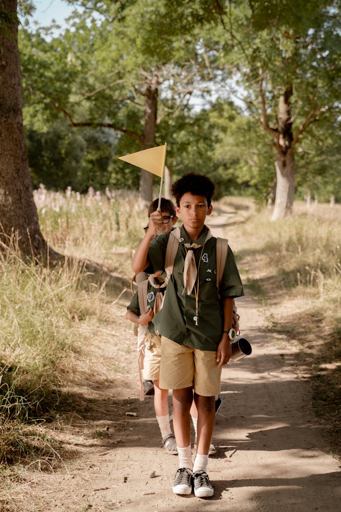 Three young scouts in uniform hiking along a forest trail holding a flag on a sunny day.